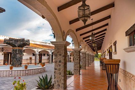 Courtyard with stone columns, arched walkways, and a water fountain under a cloudy sky.