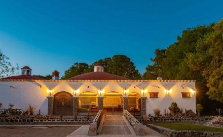 White building with arched windows, lit by outdoor lights, under a blue sky.