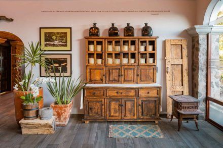 Rustic wooden cabinet with candles, framed art, and plants in a room with wood flooring.