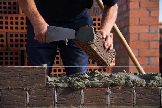 Bricklayer laying bricks, applying mortar with a trowel, outdoors.