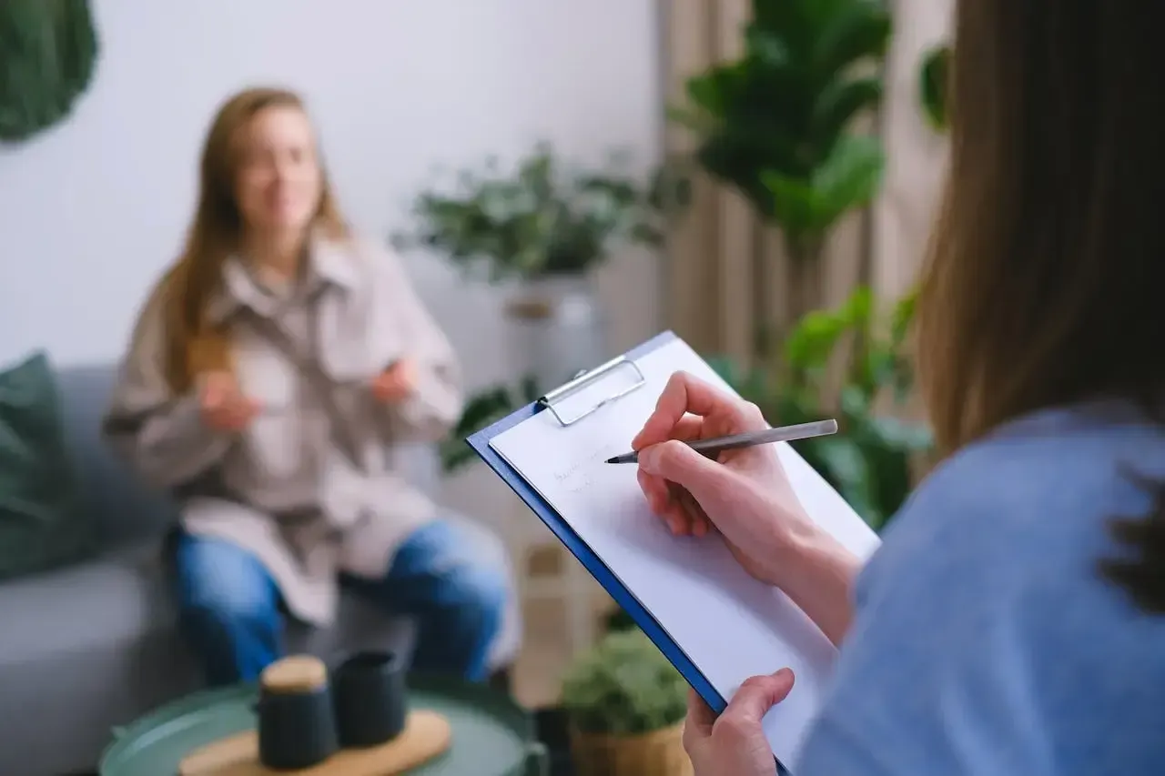 A woman writes on a notepad, while another woman talks to her