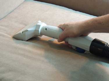 A person is cleaning a couch with a vacuum cleaner.