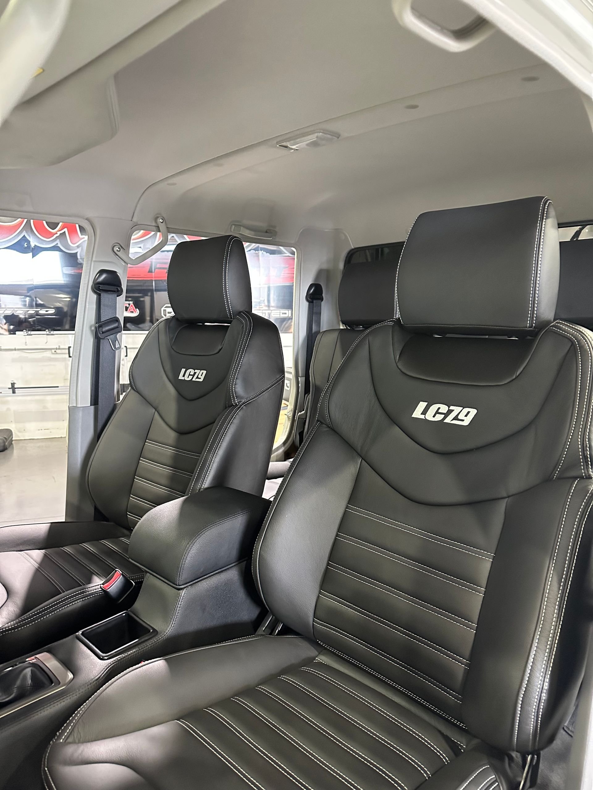 Two black leather racing seats inside a van, with white stitching and embroidered logos. — Outback Auto NT in Berrimah, NT