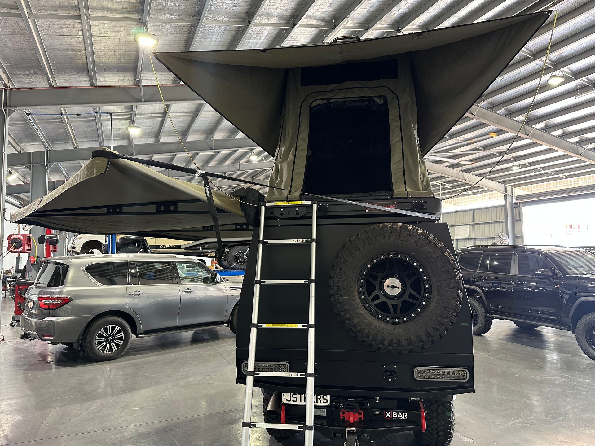 Off-road camper truck with rooftop tent and ladder parked indoors under a metal roof — Outback Auto NT in Berrimah, NT