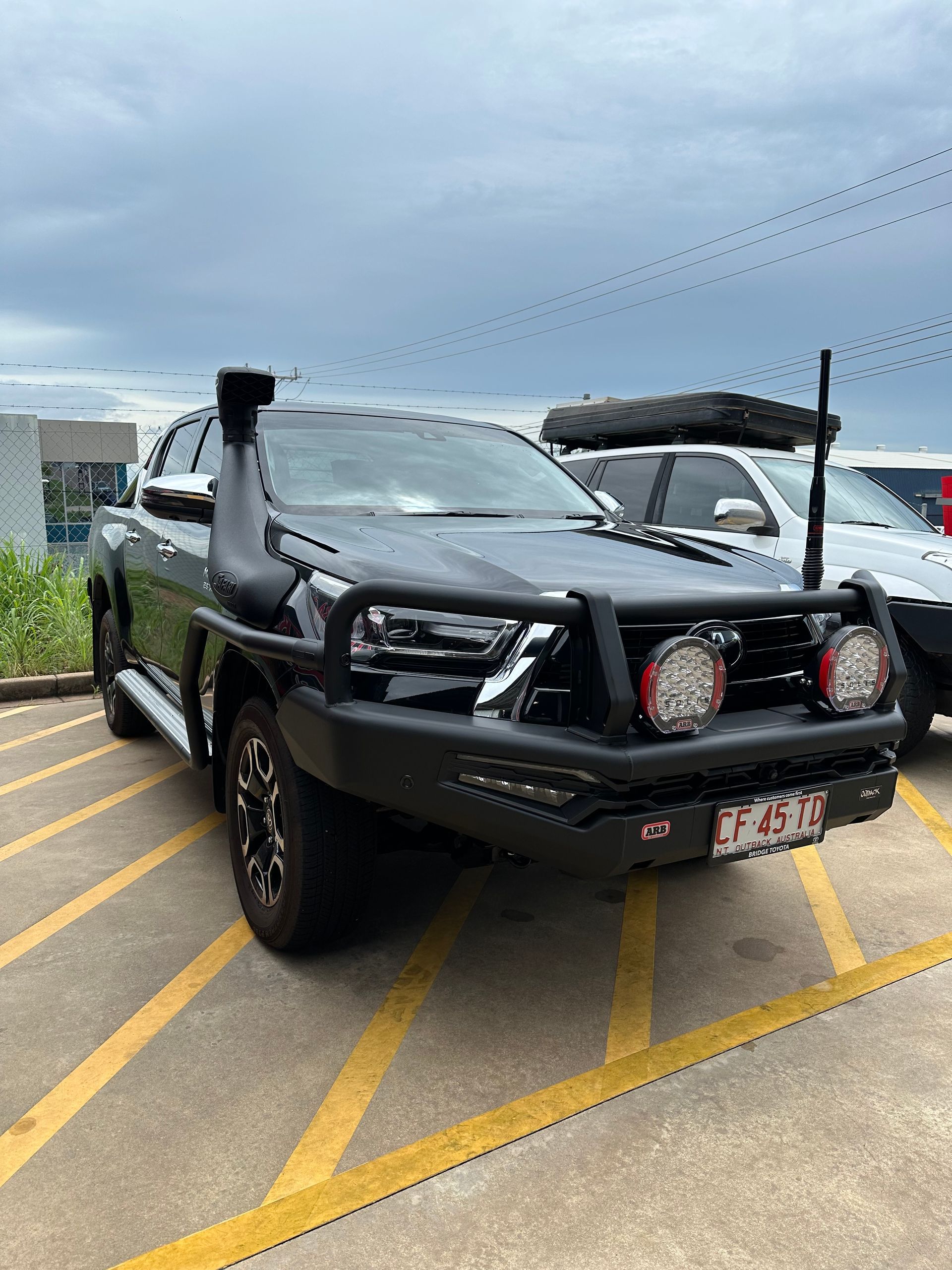 Black off-road pickup truck parked in a lot, with bull bar and spotlights under a cloudy sky — Outback Auto NT in Berrimah, NT