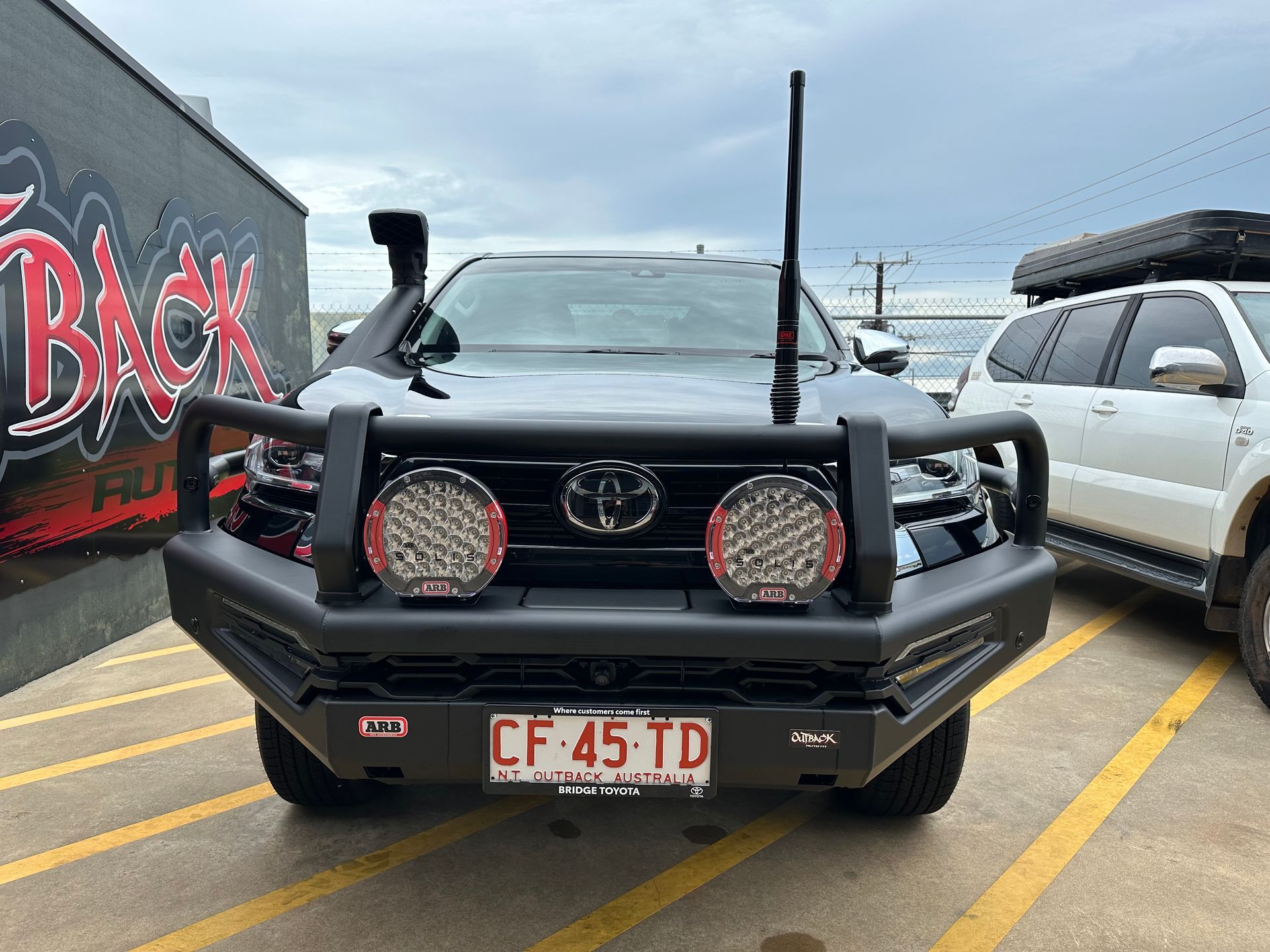 Black Toyota truck with bull bar and snorkel parked in a lot beside a graffiti wall and SUV — Outback Auto NT in Berrimah, NT