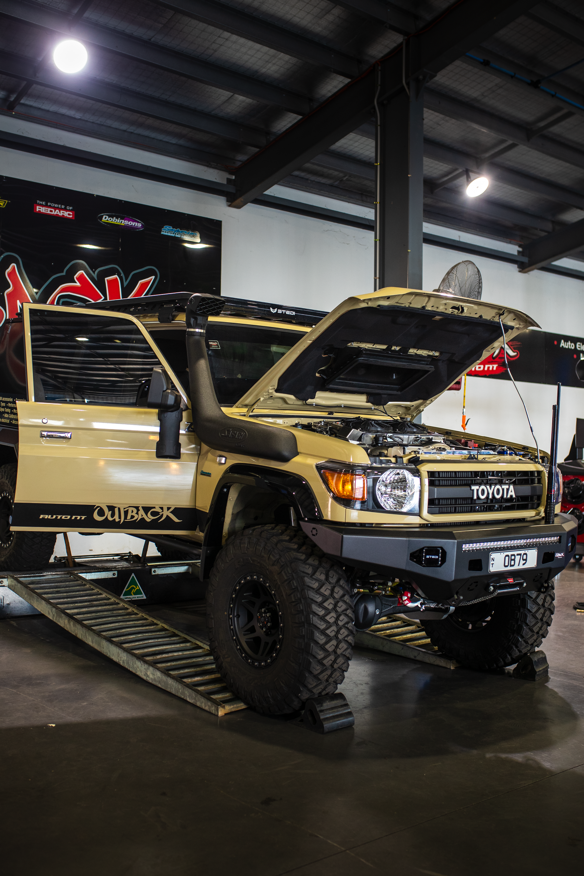 Modified yellow off-road truck on display indoors, with hood and doors open, large tires visible. — Outback Auto NT in Berrimah, NT