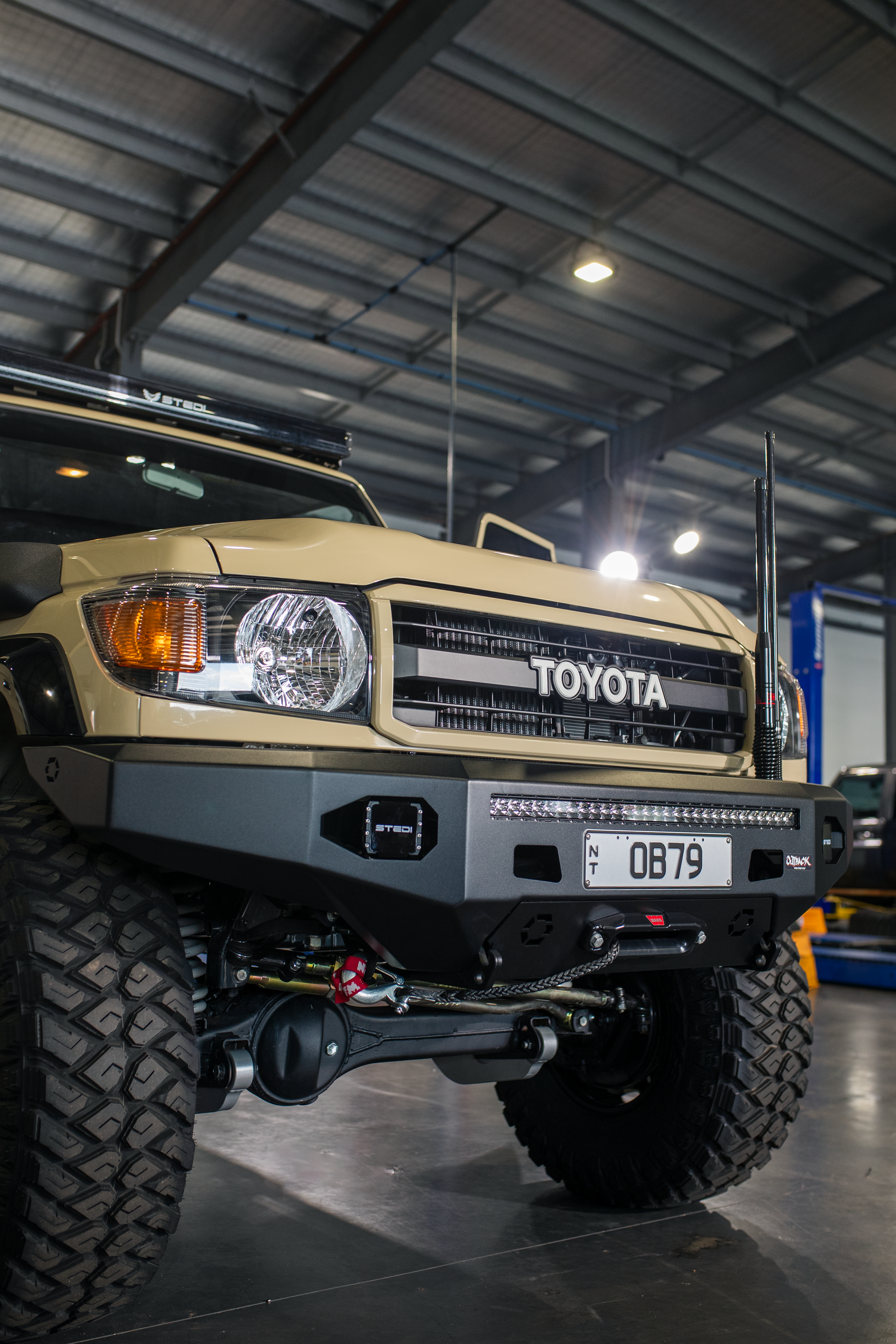 Lifted beige Toyota truck in a garage, viewed from the front with oversized tires and off-road bumper. — Outback Auto NT in Berrimah, NT