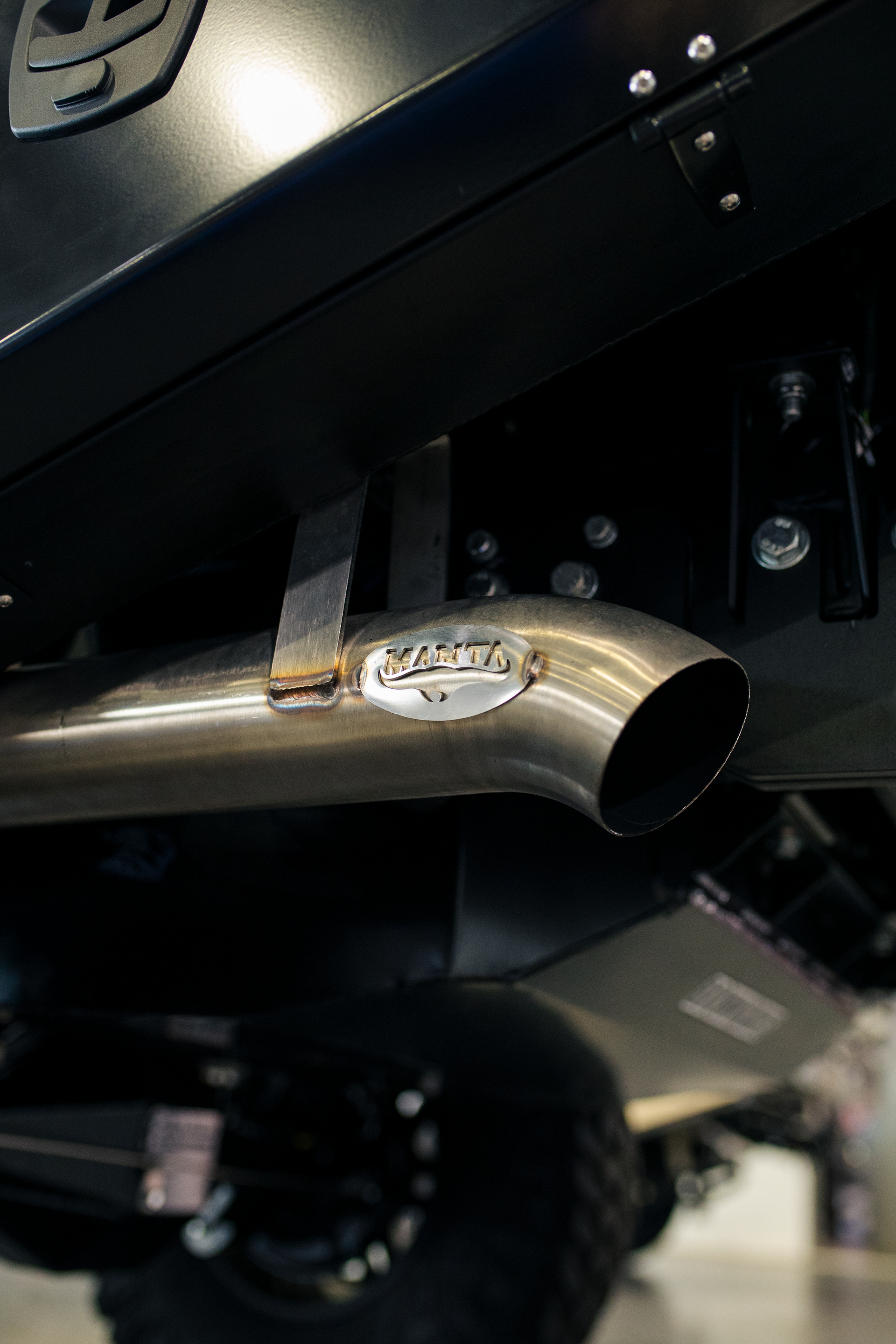 Close-up of a silver exhaust pipe under a black vehicle, with a wheel visible in the background. — Outback Auto NT in Berrimah, NT