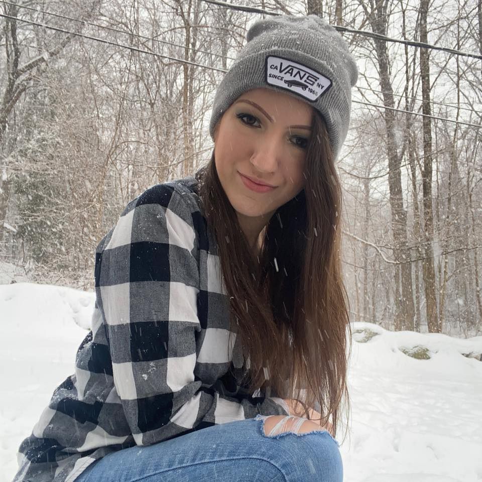 A girl wearing a vans hat is sitting in the snow