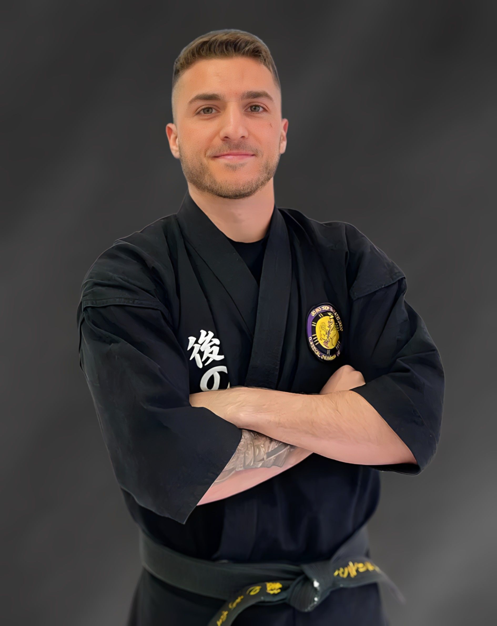 A man in a black karate uniform is standing with his arms crossed.
