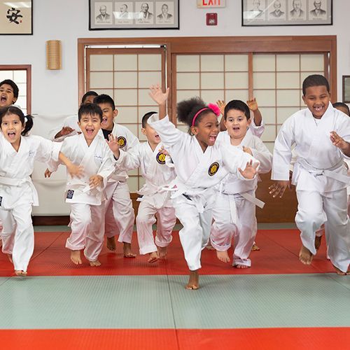 A group of children in white karate uniforms are running on a mat