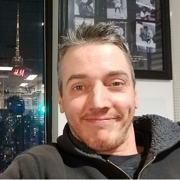 A man is taking a selfie in front of a wall with pictures on it.