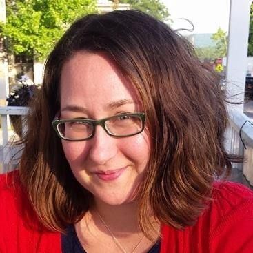 A woman wearing glasses and a red sweater is smiling for the camera.