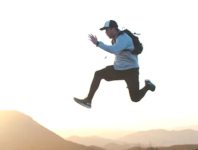 A man with a backpack is jumping in the air.