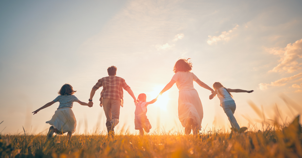 Family of five running together through a field toward the sunset, holding hands.