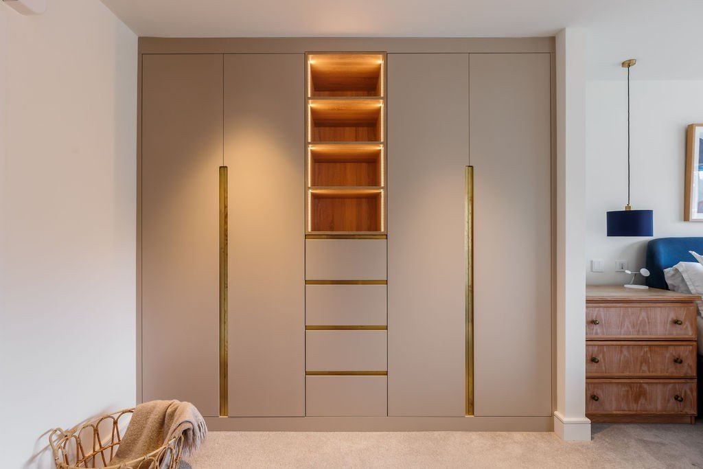 Beige wardrobe with gold handles and built-in shelves, warm lighting, in a bedroom setting.