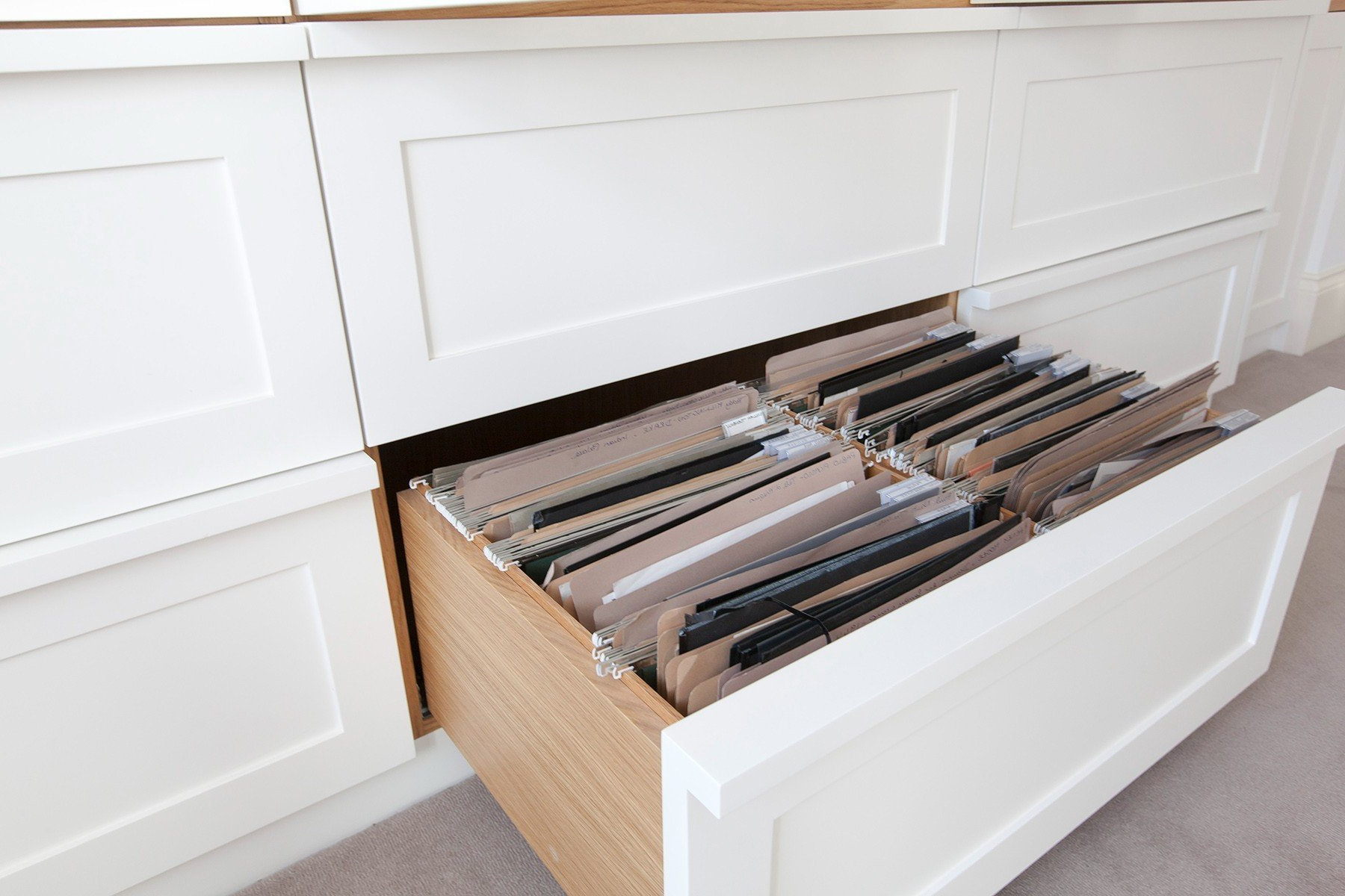 Open file drawer with hanging folders in a white cabinet under a desk.