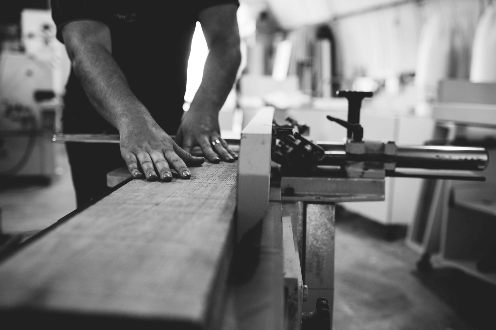 A person's hands guide a wooden plank across a woodworking machine in a workshop.