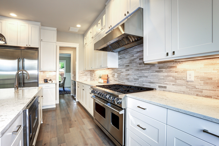 A well-lit kitchen with white cabinets and silver appliances. 