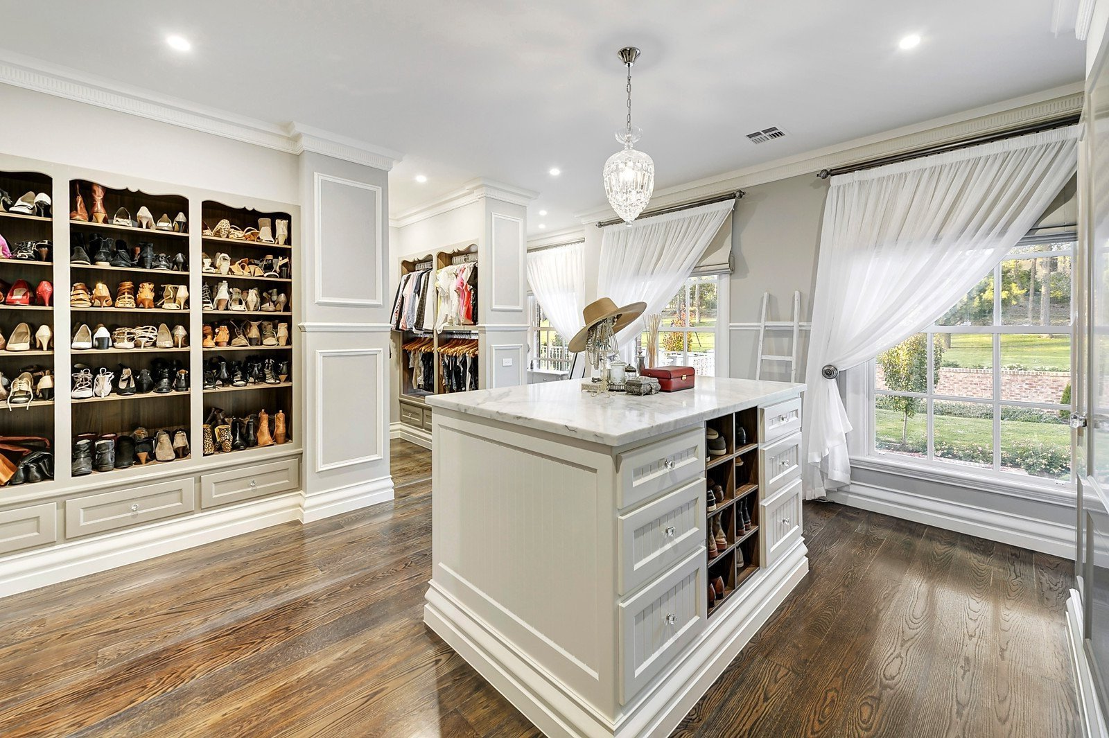 A brightly lit room with white cabinetry along the wall shelved with shoes and a white furniture in the middle of the room with storage drawers. 