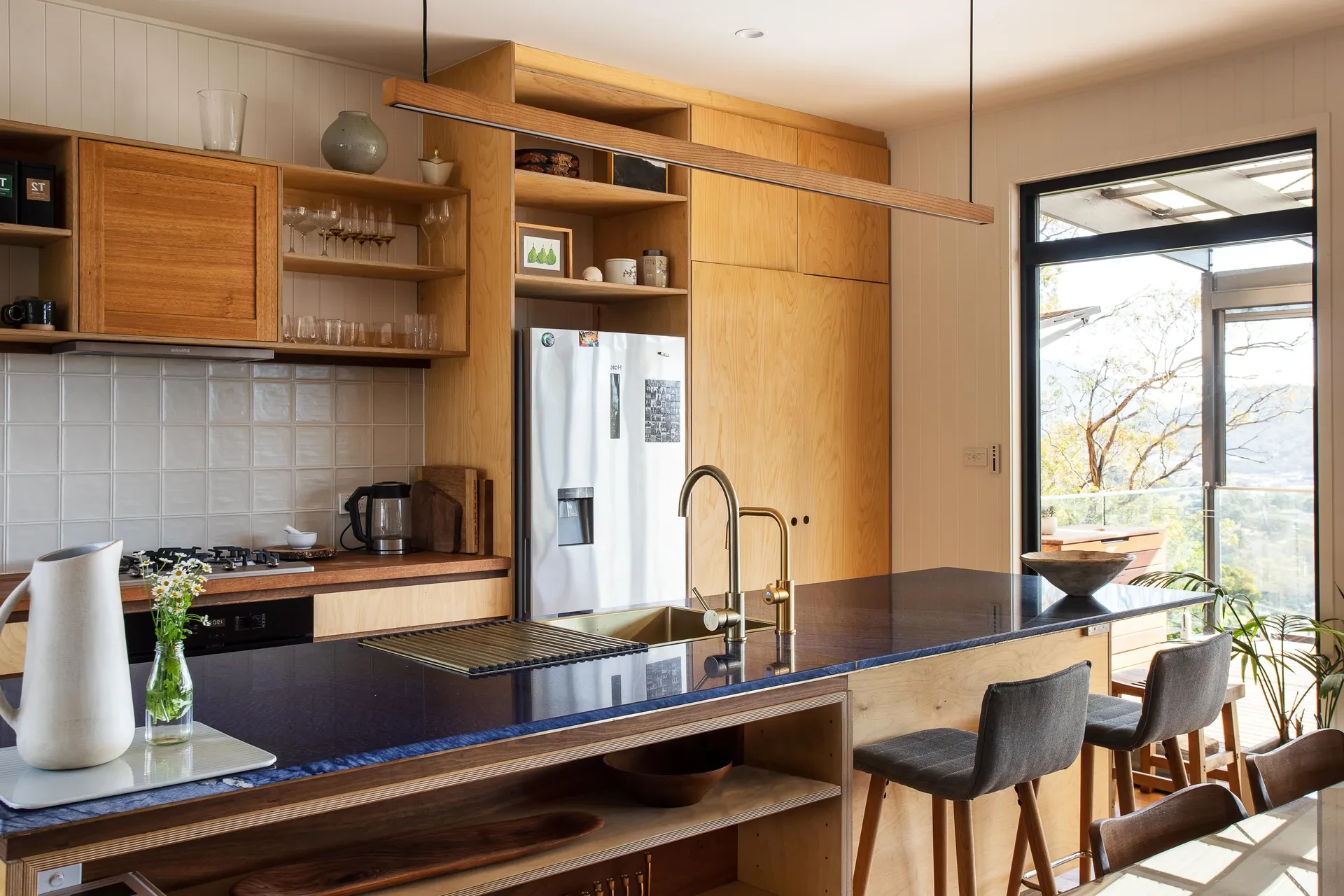 An open-plan kitchen with wooden cabinetry, black benchtop and silver appliances.