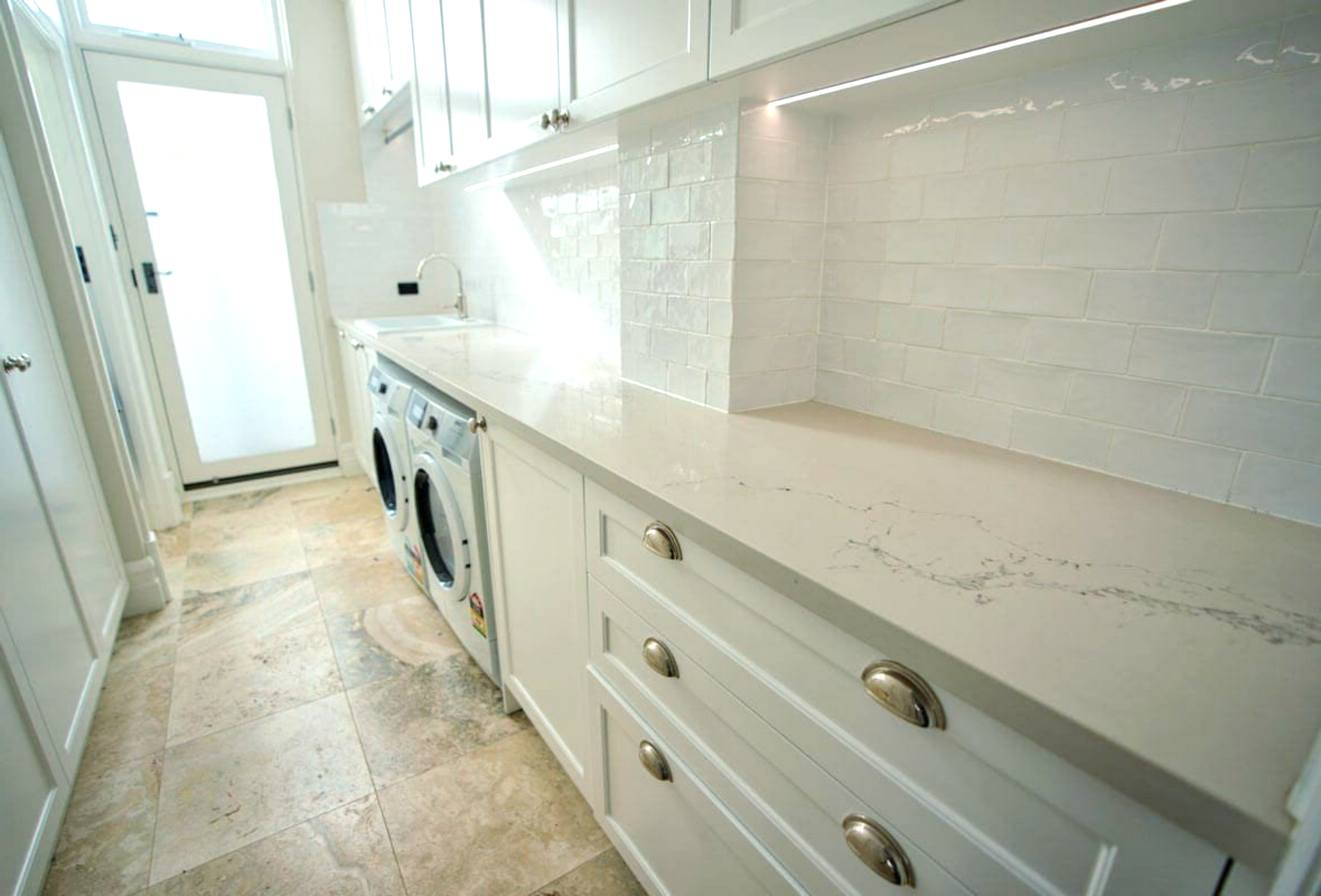 A laundry area with two washing machines and white cabinetry.