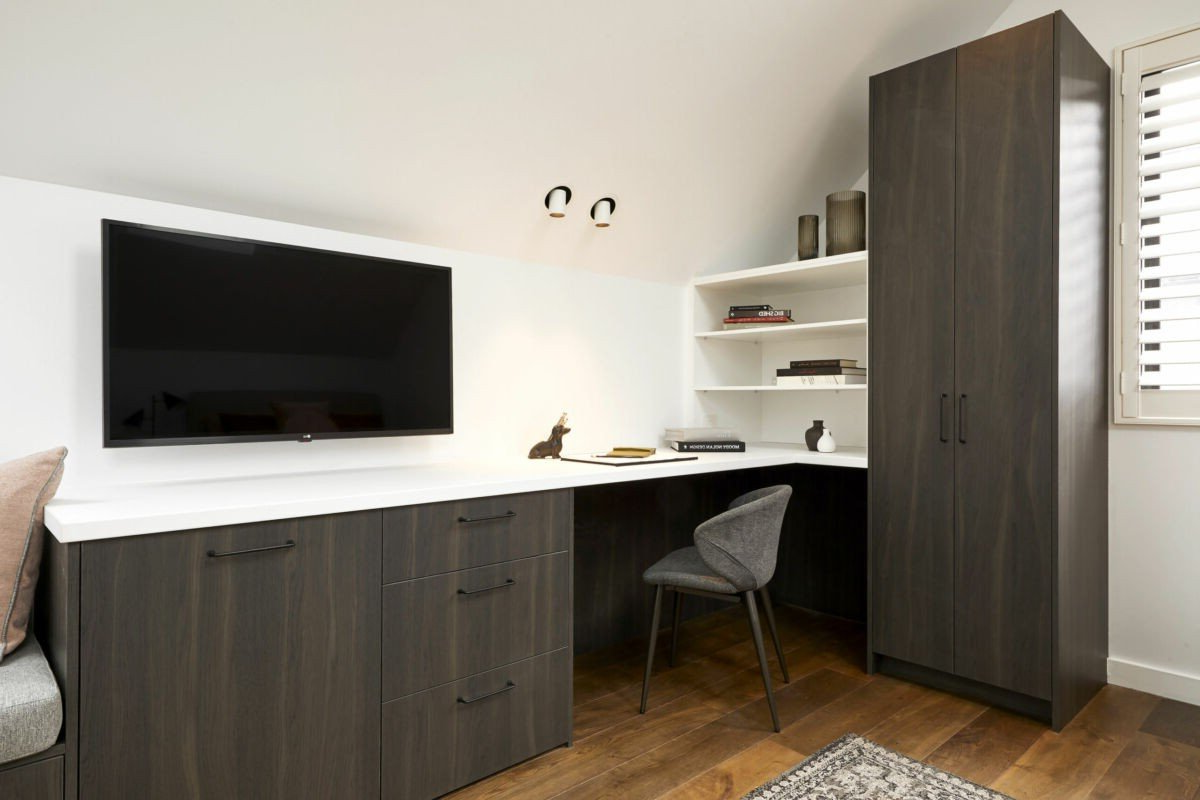 A room with a desk, chair, television and a wardrobe.