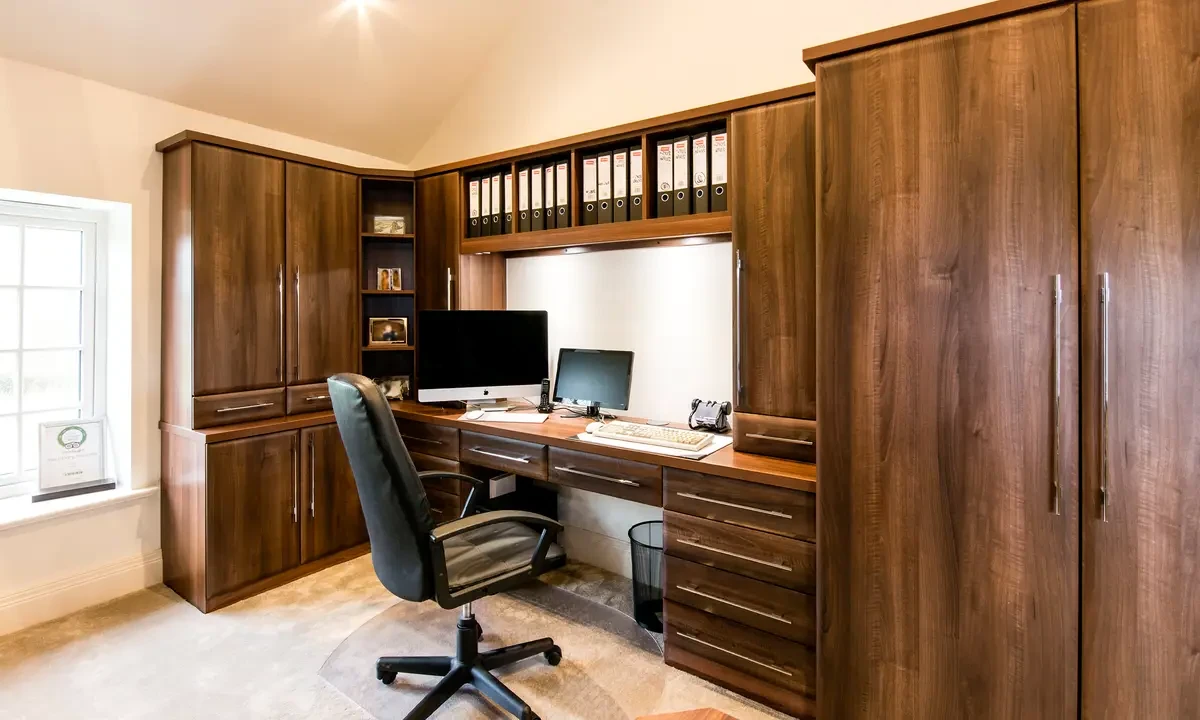 A home office with a desk, chair and computer and brown wooden cabinets.