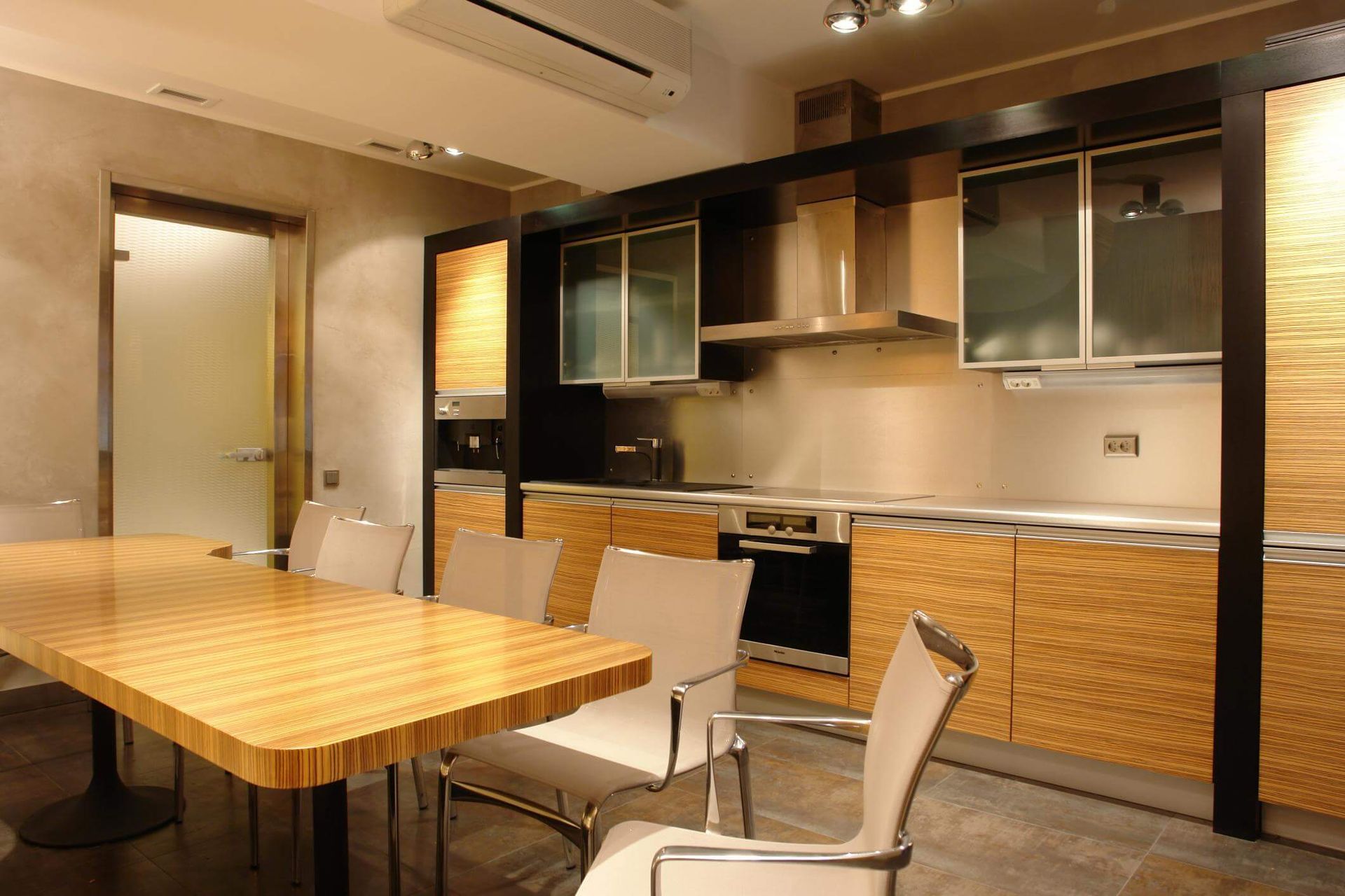 A kitchen with light brown cabinets, grey appliances, light brown table and white chairs.  