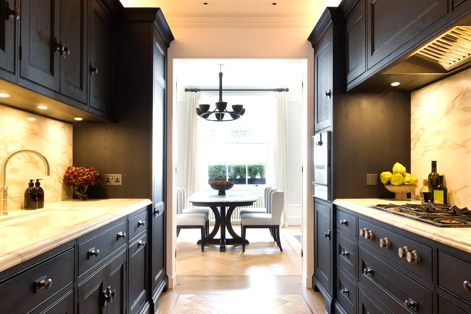 Dark kitchen with cabinets, marble countertops, and a table setting in the background.