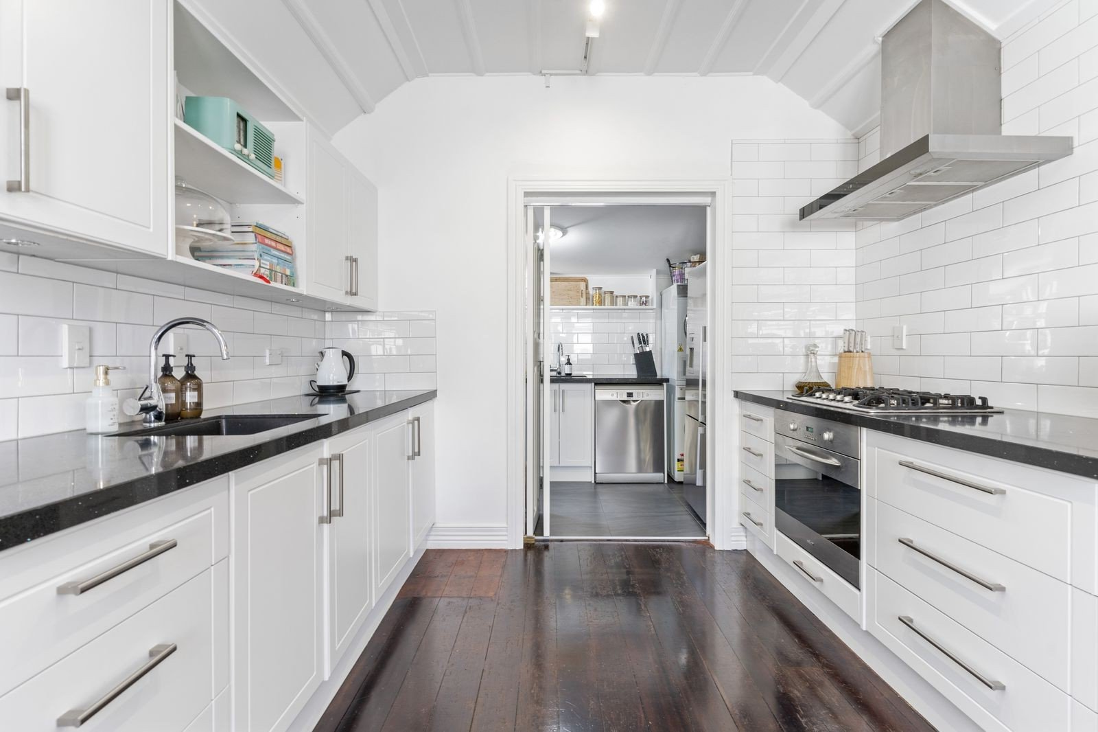 White kitchen with black countertops, stainless steel appliances, and a doorway to another room.