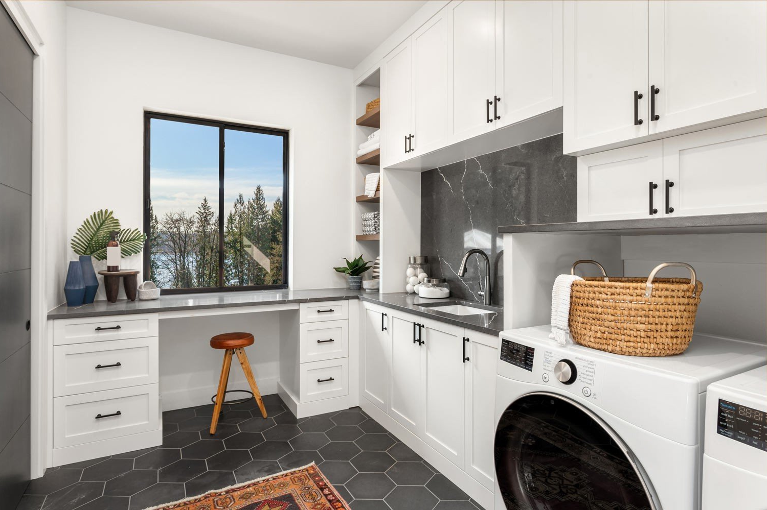 Modern laundry room with white cabinets, black accents, washer, and workspace by a window.