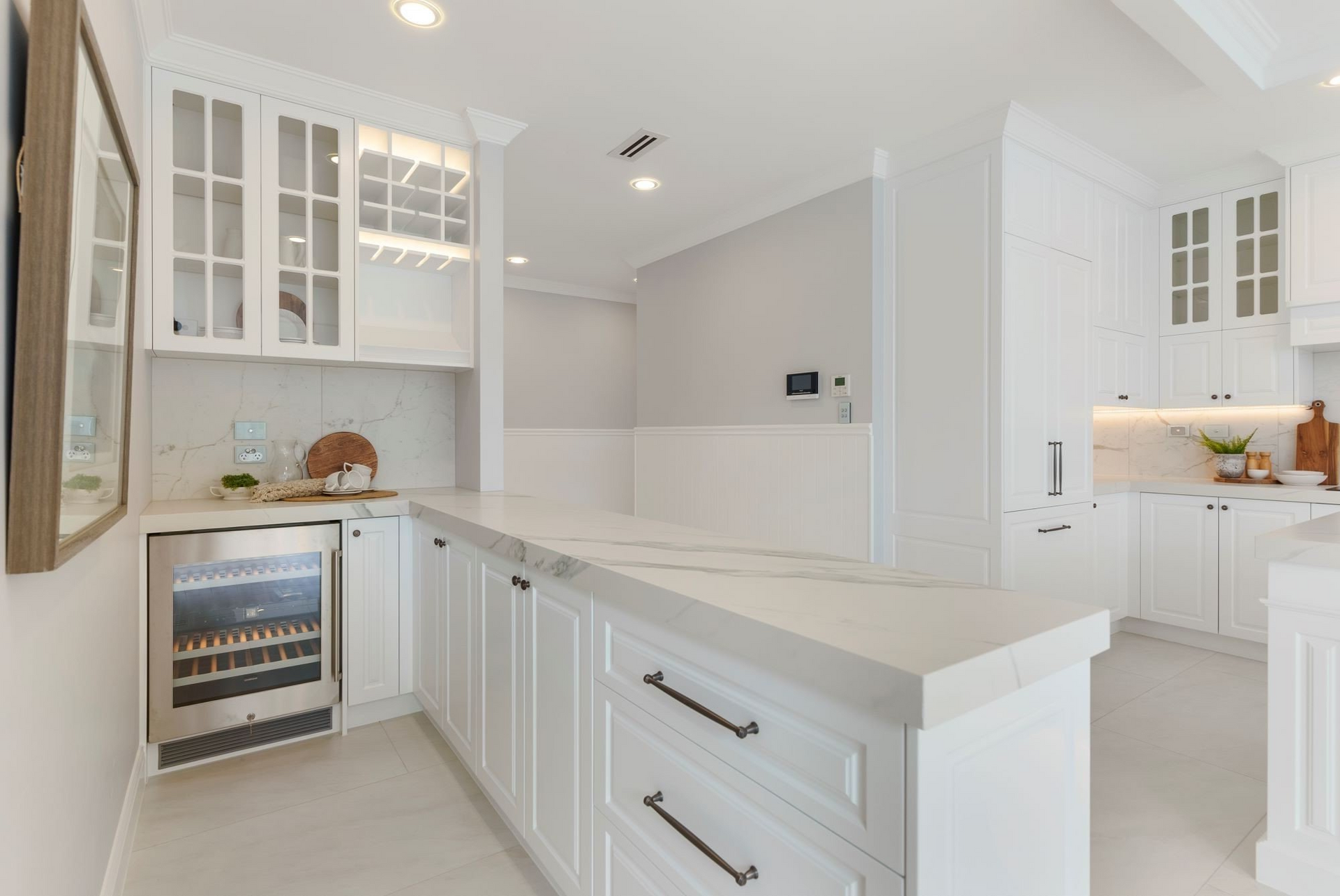 A kitchen with white cabinets, granite counter tops, stainless steel appliances and a wine refrigerator.