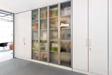 a room with tall white shelves with doors shut and book shelves with blurry transparent doors shut