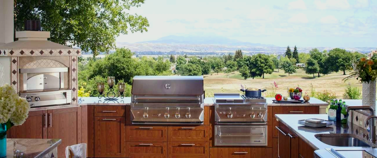 Outdoor kitchen with a grill, oven, and sink overlooking a scenic landscape.