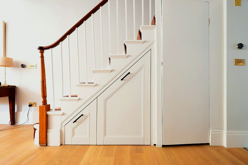 A white staircase with a wooden railing and a door underneath it,
