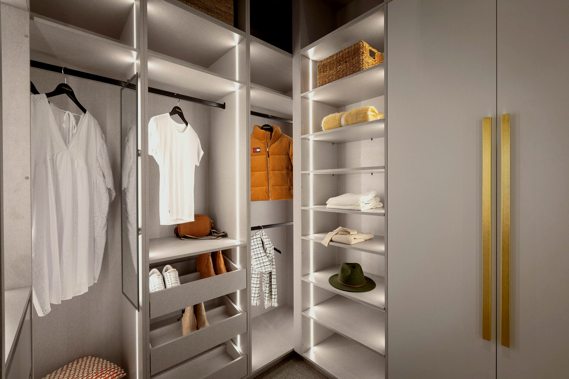 Walk-in closet with clothes, shoes, and shelves. Lit with bright lights; features grey and gold accents.