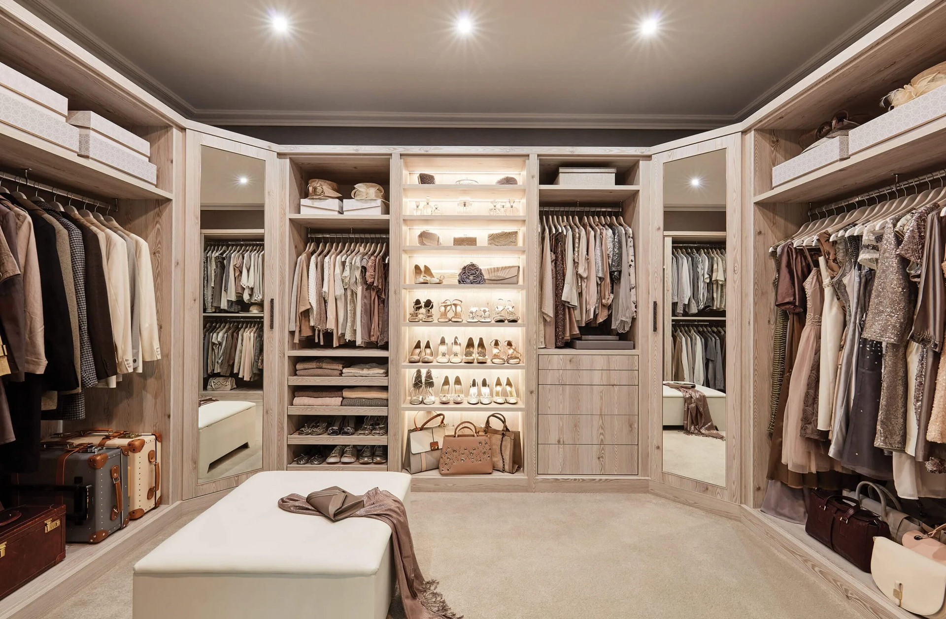 Walk-in closet with clothes, shoes, and accessories organised on shelves, racks, and in boxes. Bench in the centre.