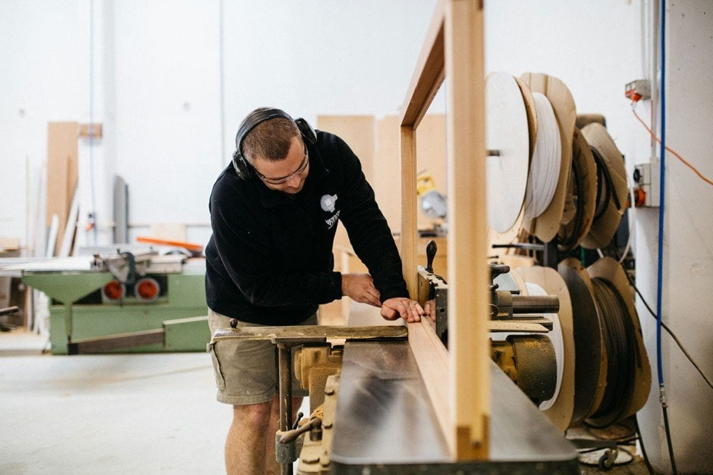 A man is cutting a piece of wood on a machine in a workshop.