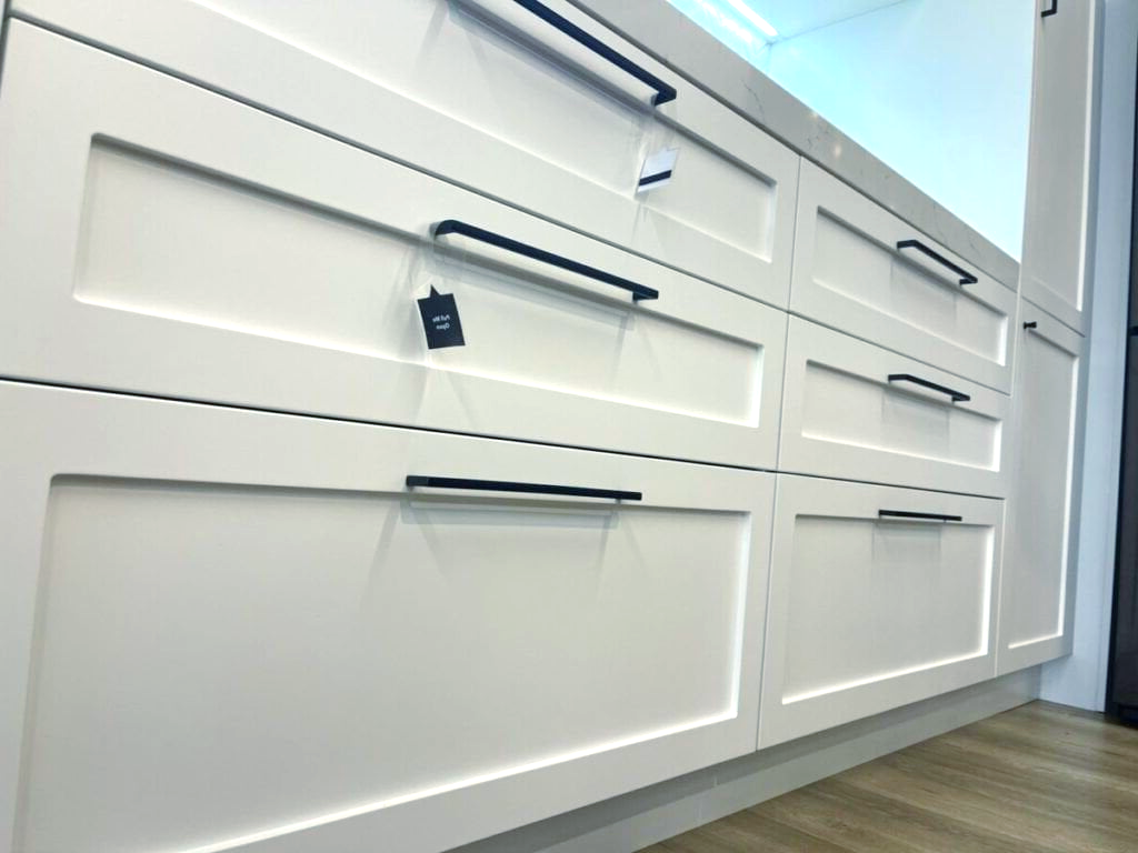 A kitchen with white cabinets and black handles.