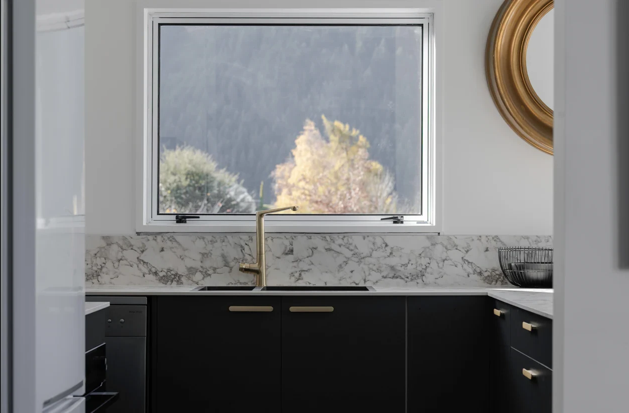 A kitchen with black cabinets, a sink, a mirror and a window.