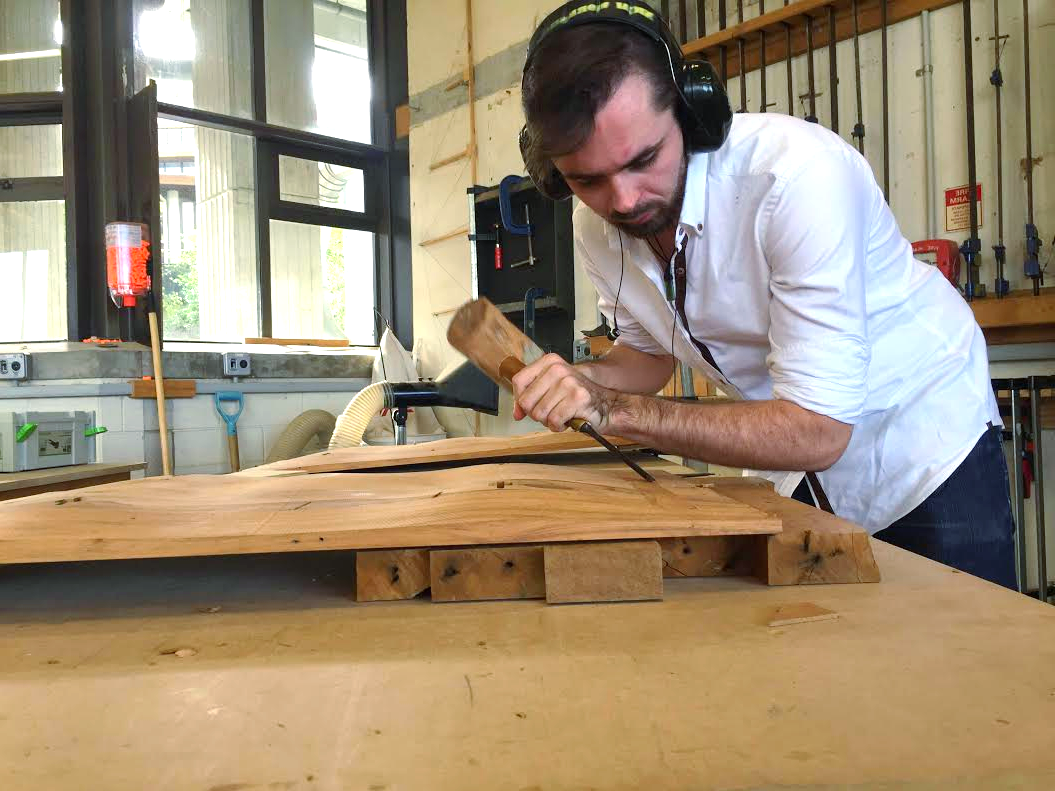 A man wearing headphones is working on a piece of wood.