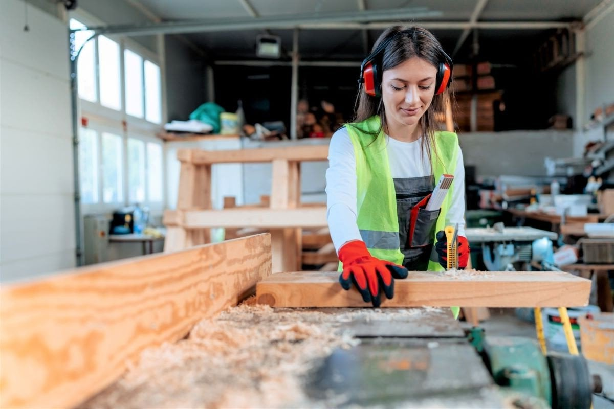A woman is cutting a piece of wood on a table saw in a workshop.