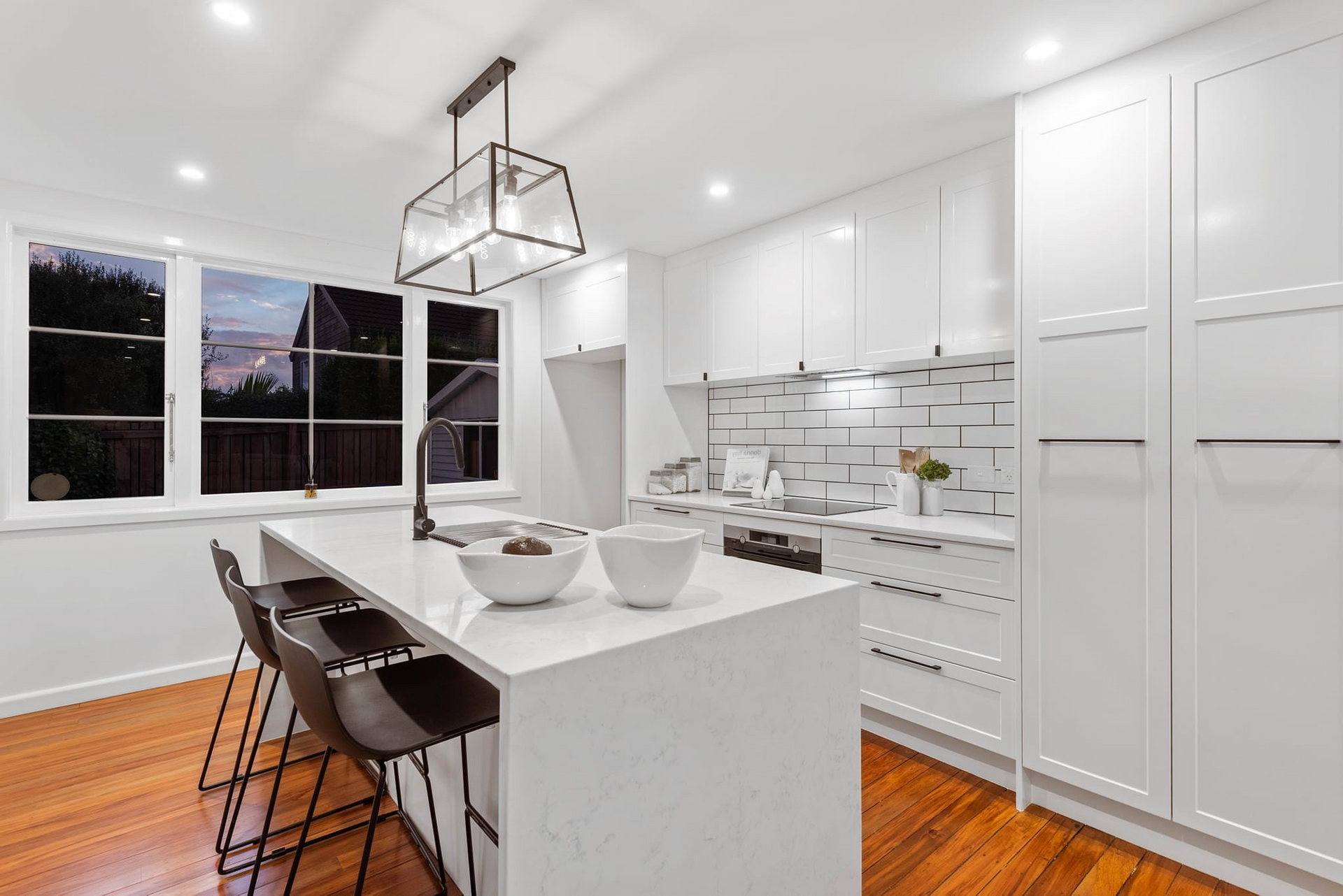 A kitchen with white cabinets and wooden floors and a large island.