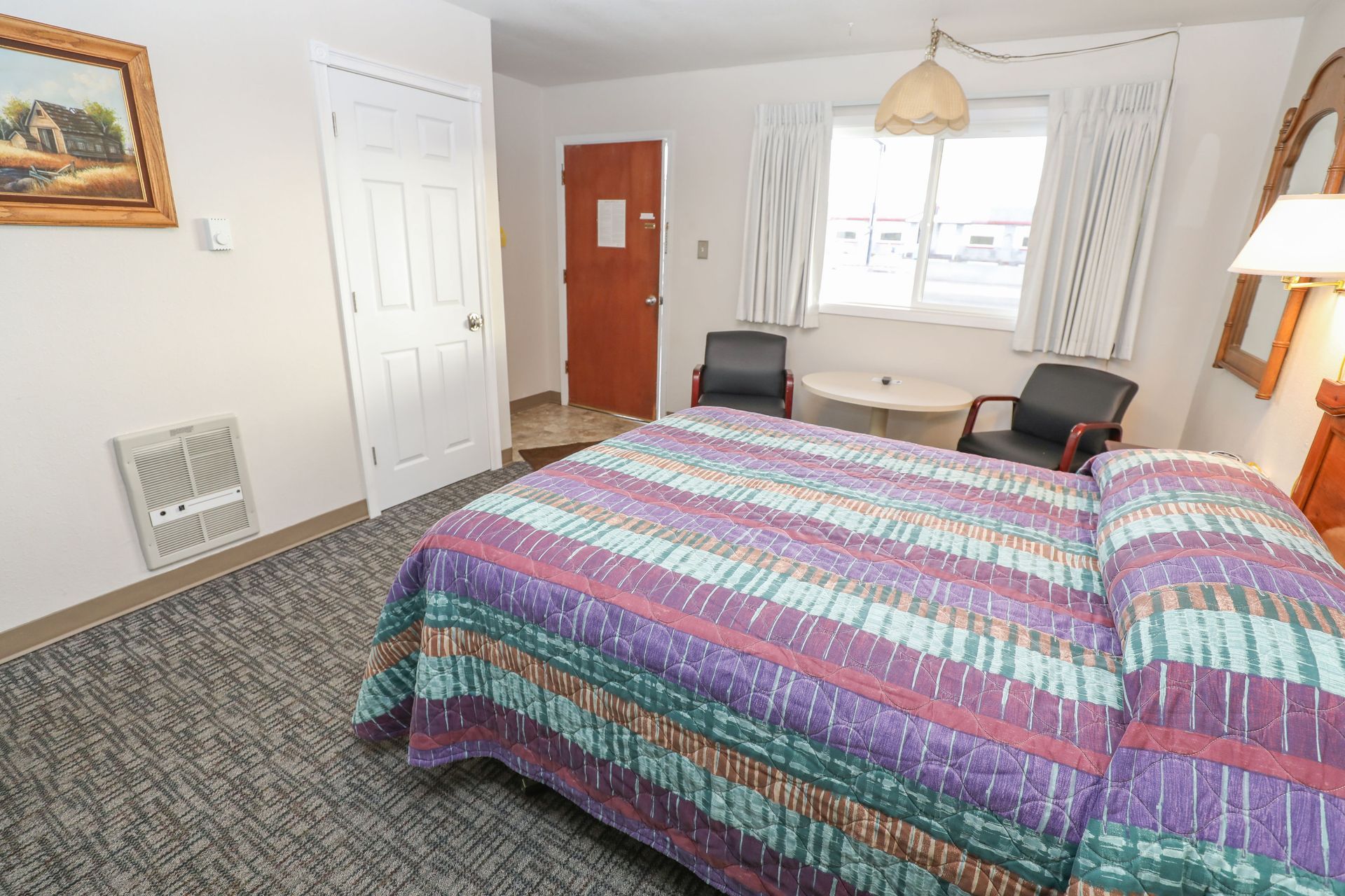 A hotel room with a king size bed , chairs and a table.