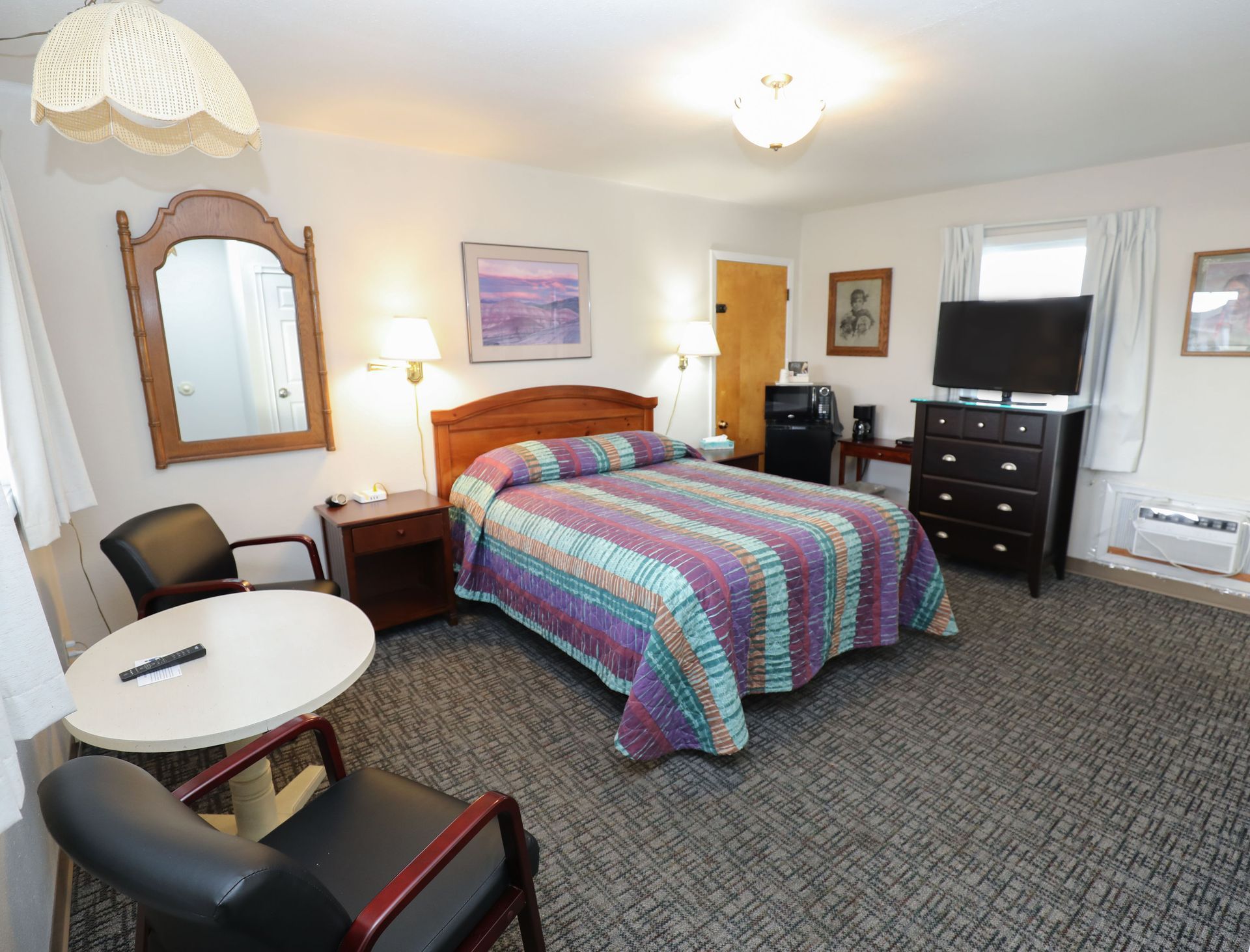 A hotel room with a king size bed , chairs , dresser and television.