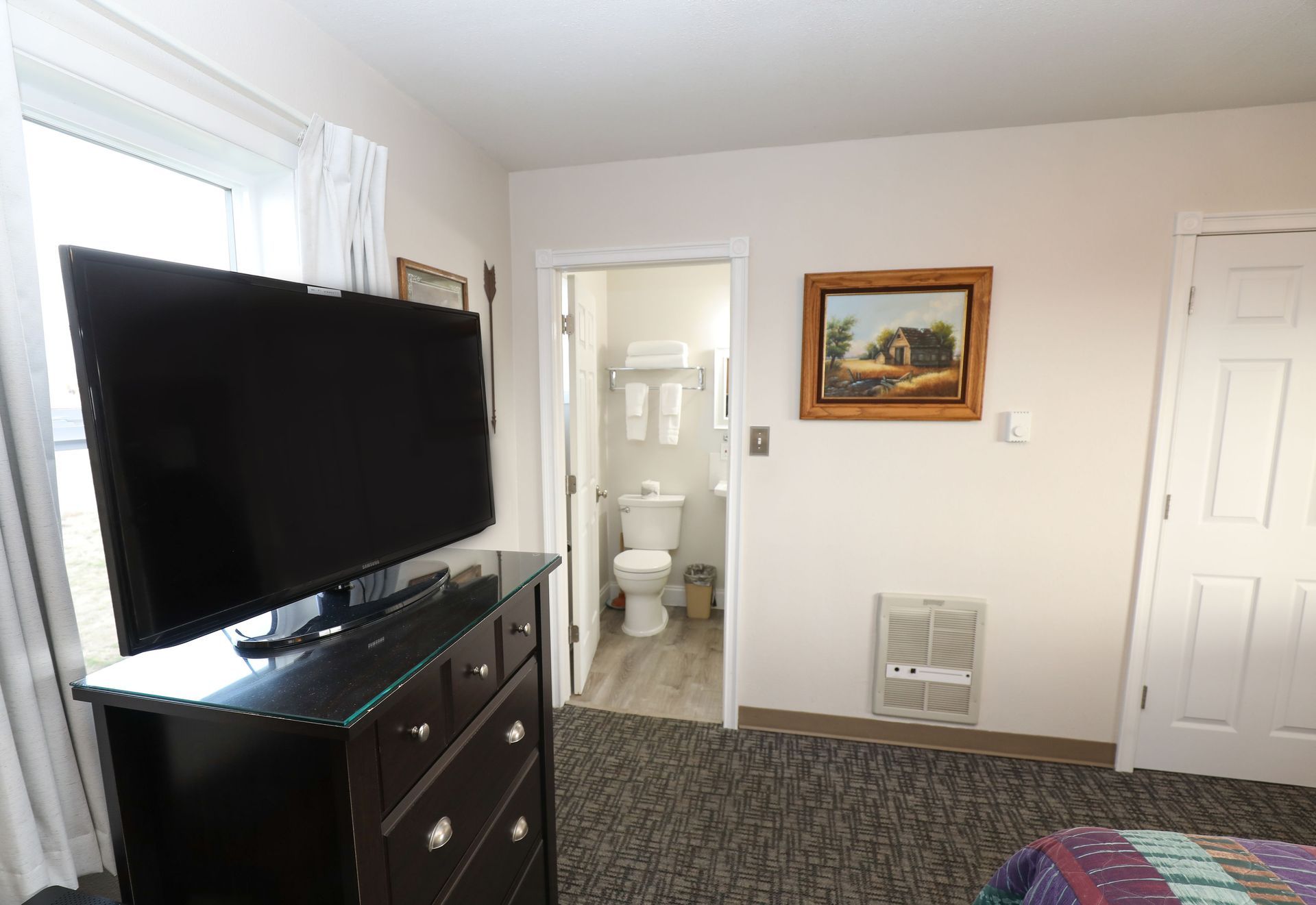A hotel room with a flat screen tv and a dresser.