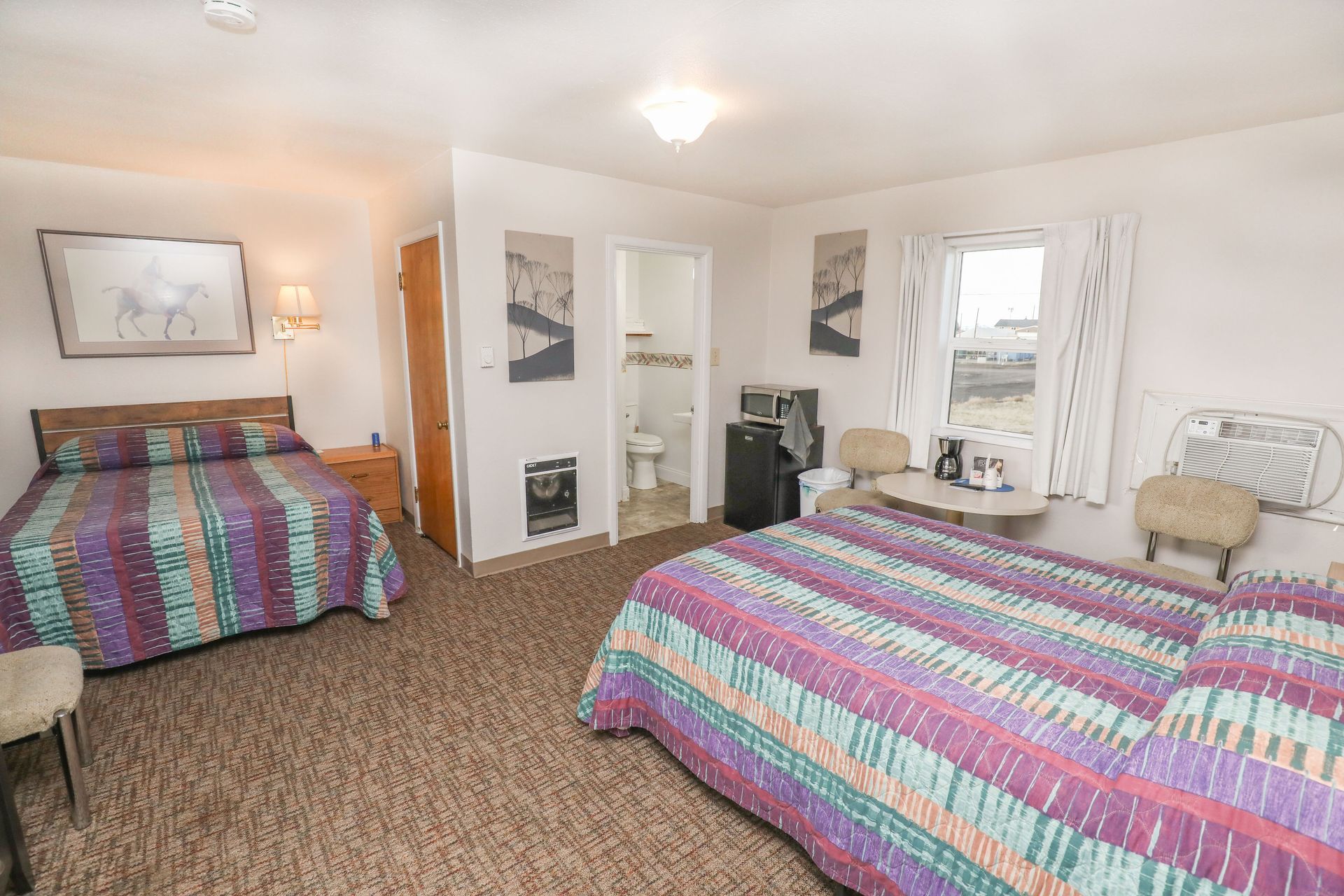 A hotel room with two beds , a table , chairs and a bathroom.