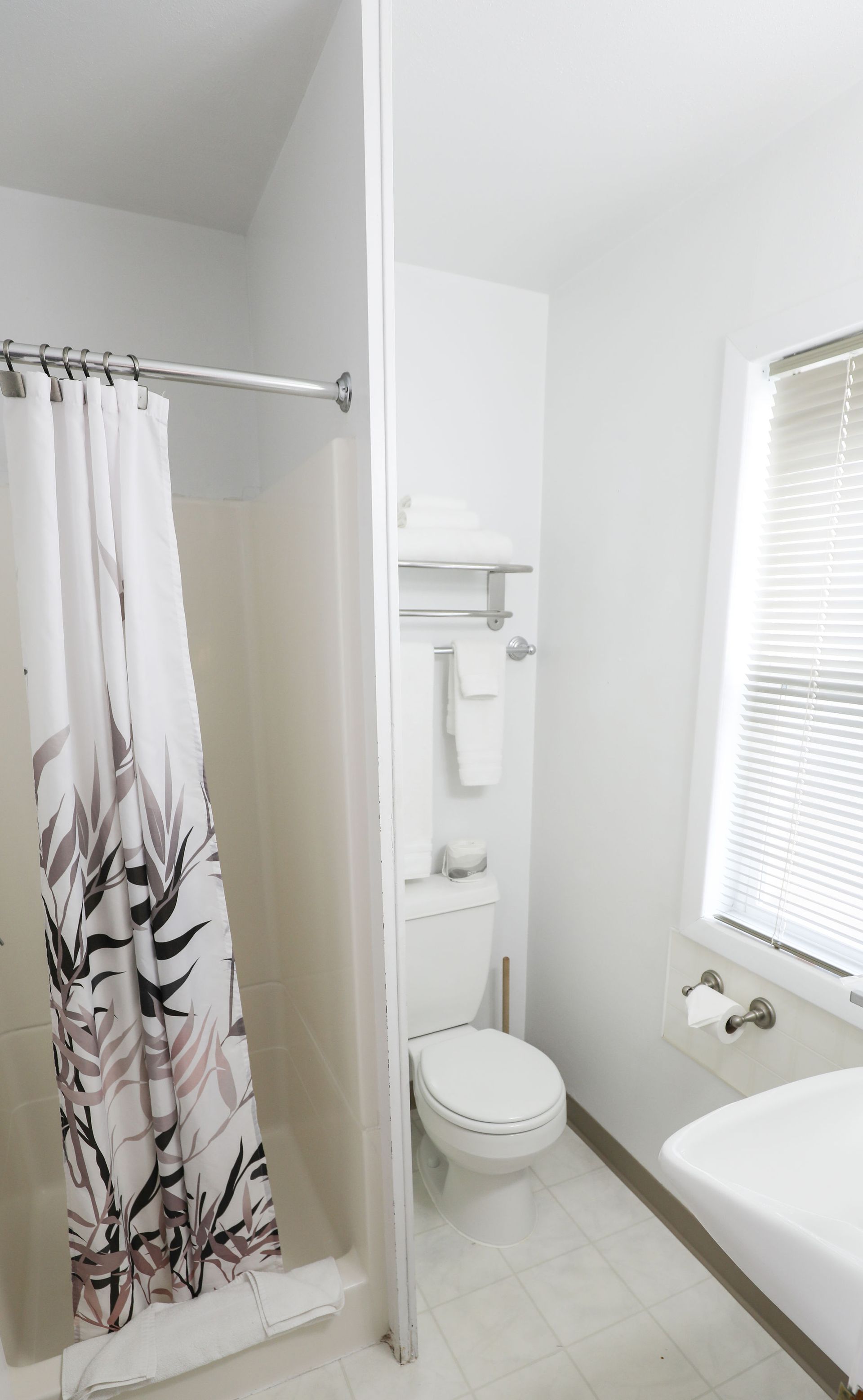 A bathroom with a toilet , sink , shower and window.
